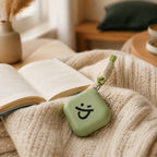 Oplaadbare handwarmer in pastelgroen op een gebreid crème plaid naast een open boek
