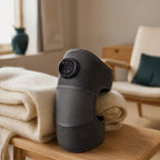 Verwarmde kniebandage in antraciet met digitaal display, op een houten bank met wollen plaid