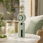 Handventilator met koelplaat in mintgroen op een witte tuintafel met een koud glas limonade
