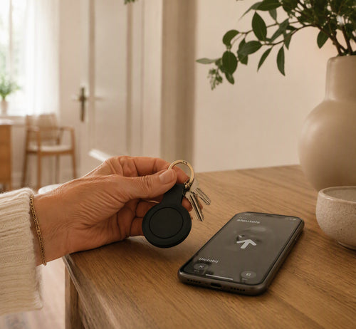 Bluetooth-sleutelvinder aan sleutelbos naast smartphone — warme Seniorslim huisstijl